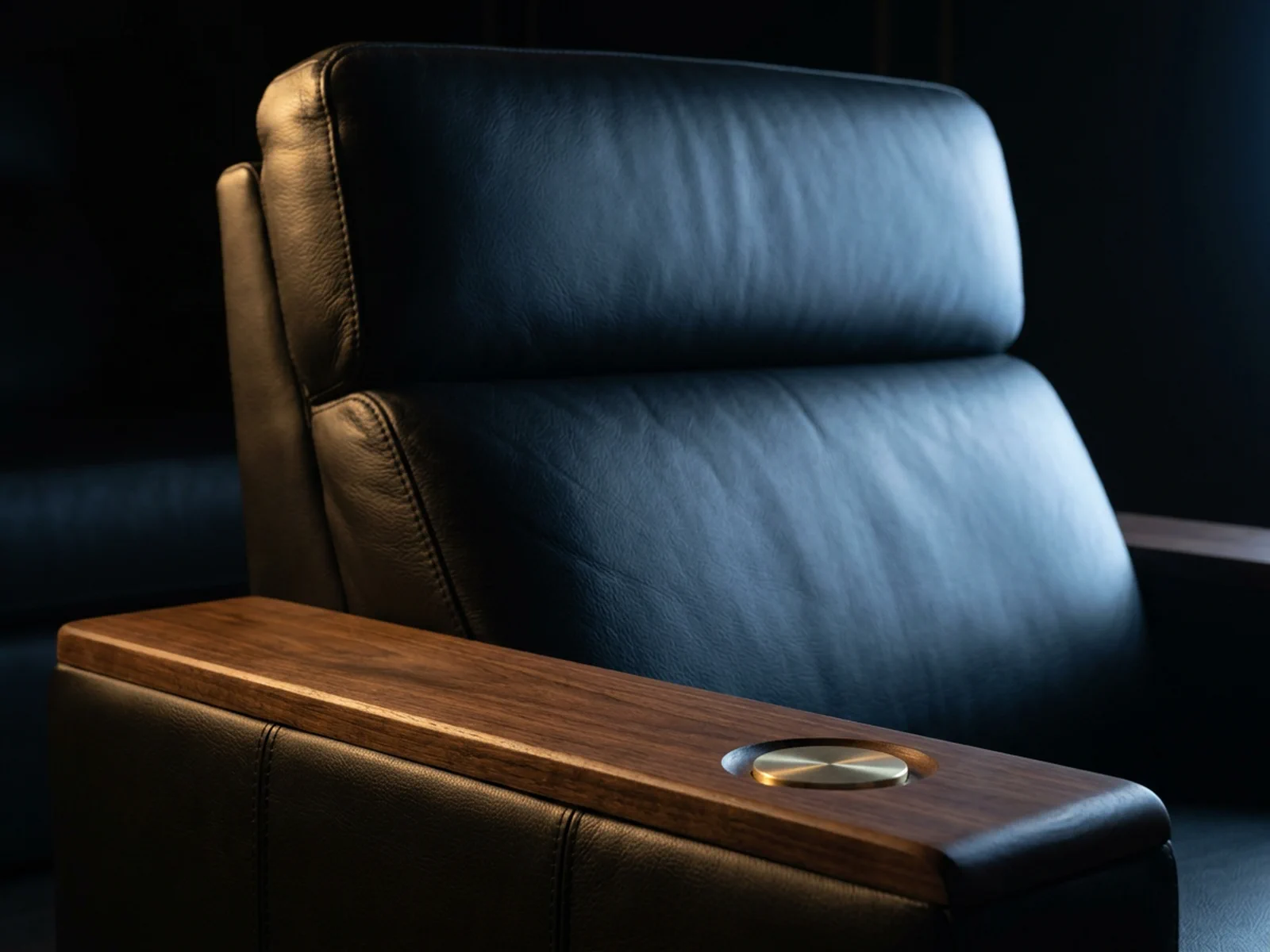 Detail of a handcrafted black leather cinema recliner with fine stitching and a walnut armrest